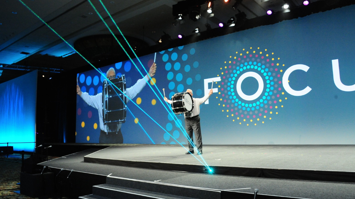 Man speaking to a large room full of people on a stage