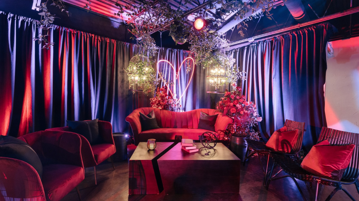 Romantic event lounge with red seating, floral décor, and neon heart lighting.