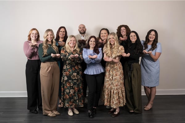 Group of coworkers standing together, smiling and holding their hands open forward, representing the idea of Give to gain