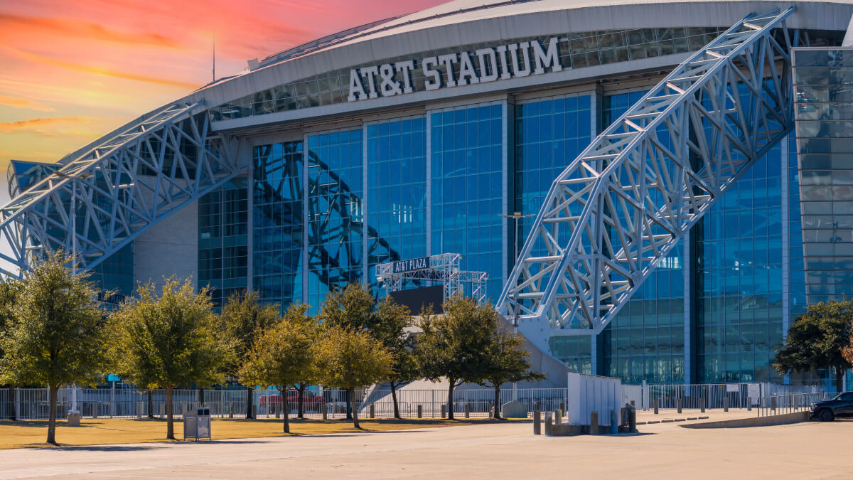Exterior view of AT&T Stadium at sunset with the stadium’s iconic steel arches and glass façade on display.
