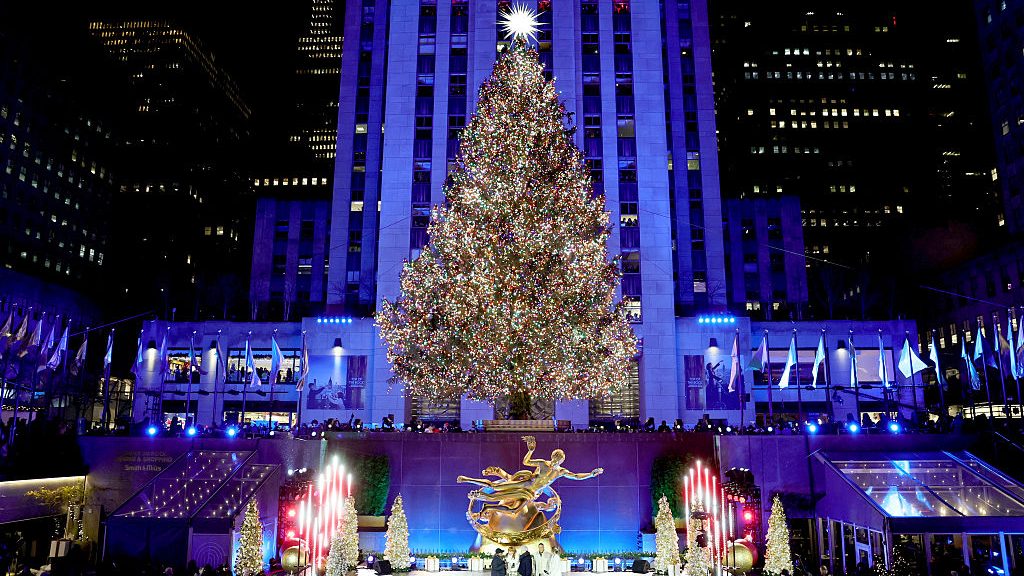 The Rockefeller Center Christmas tree glowing at night in front of 30 Rockefeller Plaza, with the golden Prometheus statue and holiday crowds below.