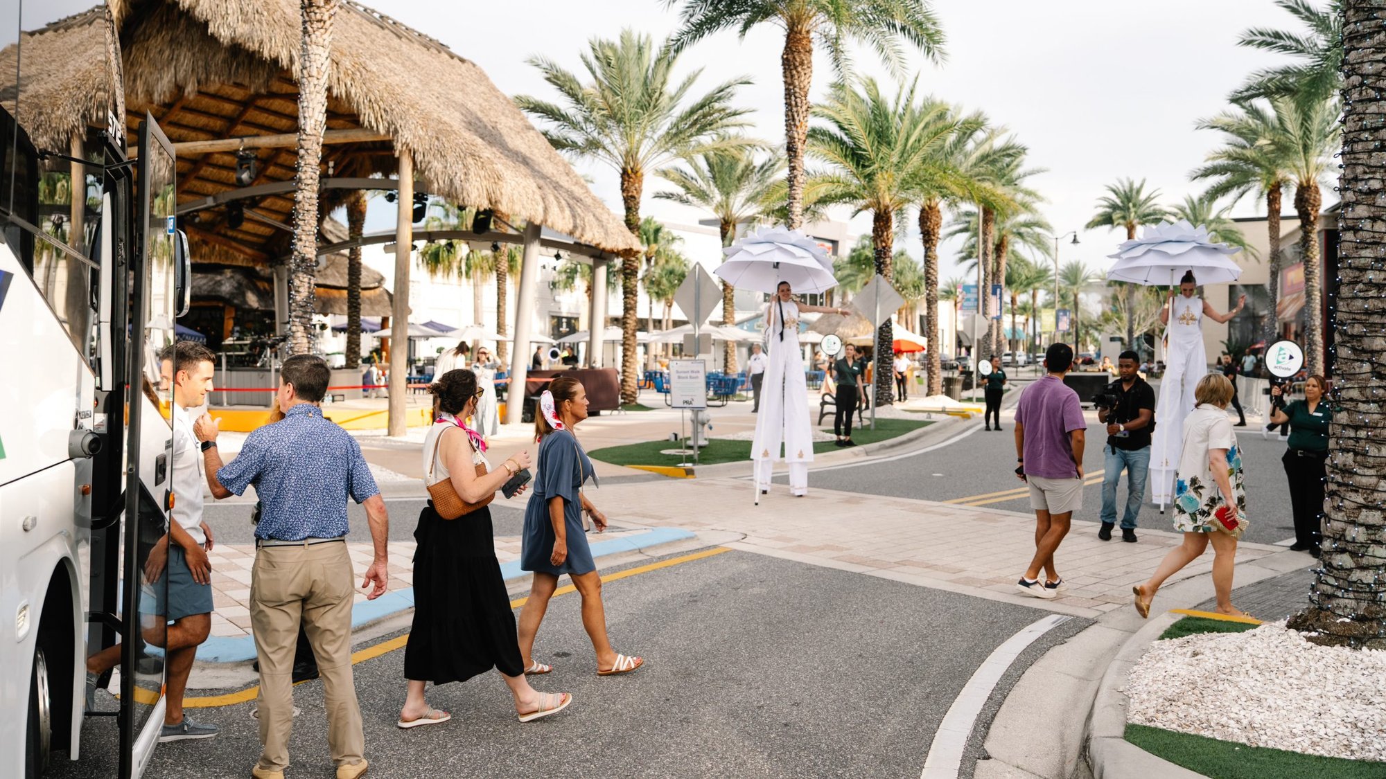 Guests arrive by motorcoach at The Promenade at Sunset Walk as stilt walkers welcome them to the outdoor Maritz Activate block party.
