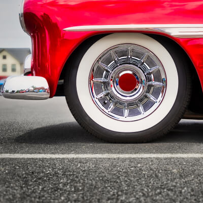 Close-up of a classic red car wheel with chrome details and whitewall tire