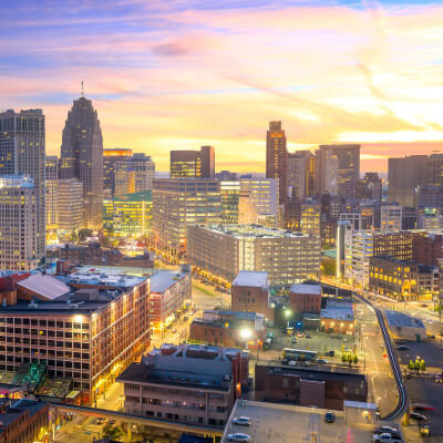 Downtown Detroit skyline at sunset with glowing city lights and warm tones.