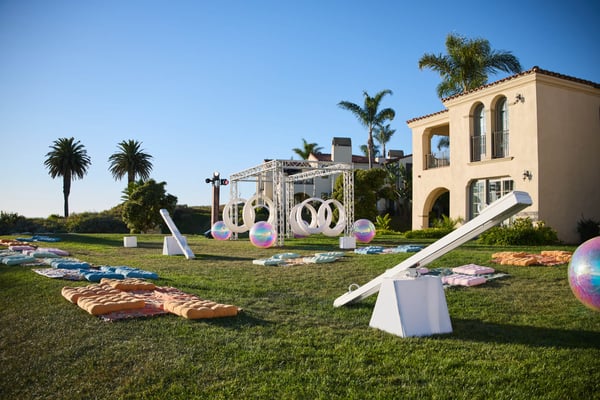 Outdoor lawn setup with games and lounge seating near a coastal villa under a clear blue sky.