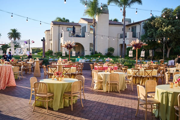 Outdoor dining area with round tables, colorful linens, and string lights in a courtyard setting.