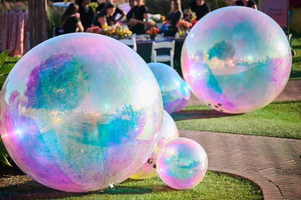 Large iridescent decorative spheres displayed on grass as part of event décor.