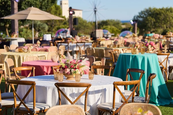 Outdoor dining tables with colorful tablecloths and floral centerpieces in a garden setting.