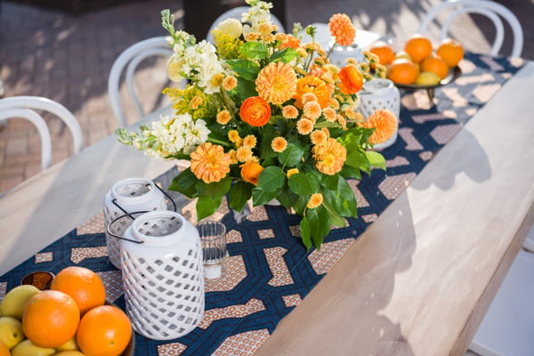 Close-up of a floral centerpiece with orange and yellow flowers on a dining table.