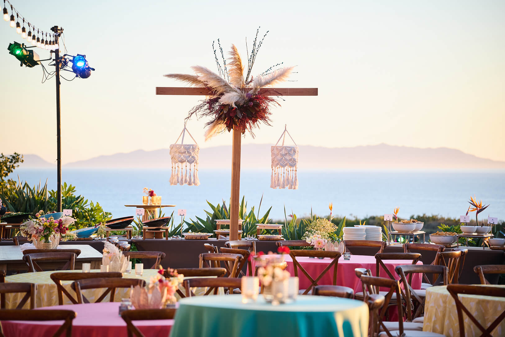 Colorful outdoor dining area with round tables, floral décor, and a decorative wooden structure set against an ocean view.