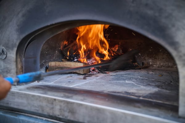 Wood-fired oven with visible flames inside, used for event catering.
