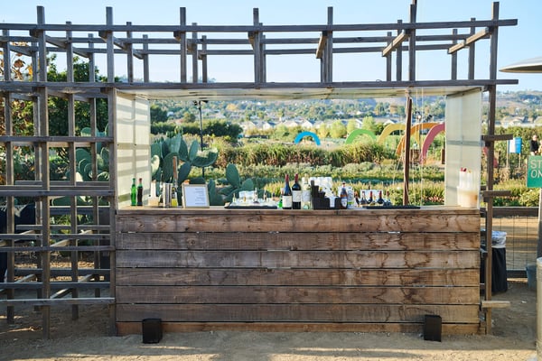 Rustic wooden bar structure set up outdoors with a vineyard view.