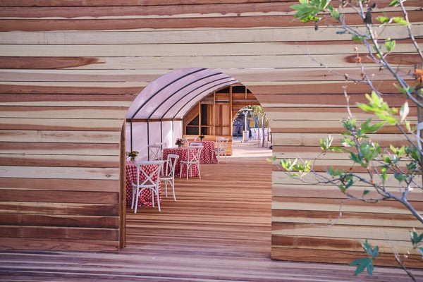 Wooden tunnel walkway with curved beams leading through an event installation.