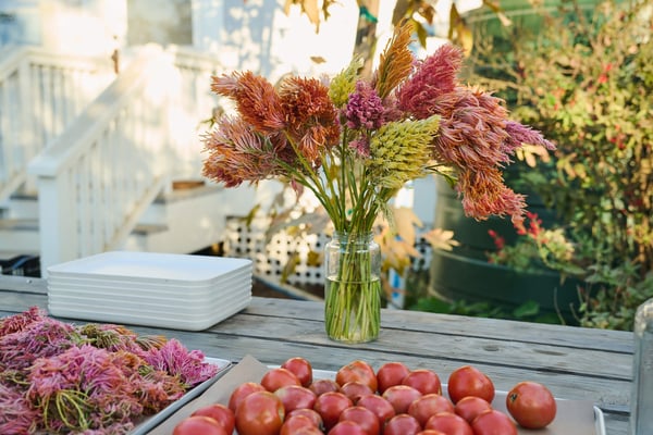 Fresh flowers and produce arranged on a table in an outdoor setting.