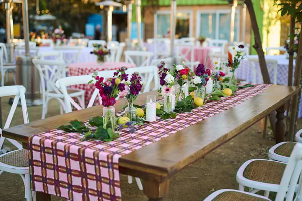 Outdoor banquet table with floral centerpieces and checkered tablecloth in a garden setting.
