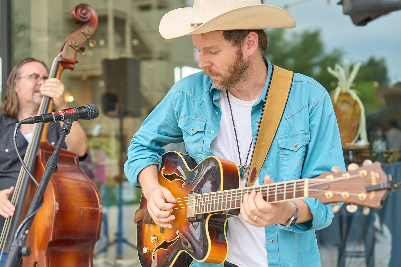 Country musician playing guitar alongside an upright bass player during a live outdoor performance.