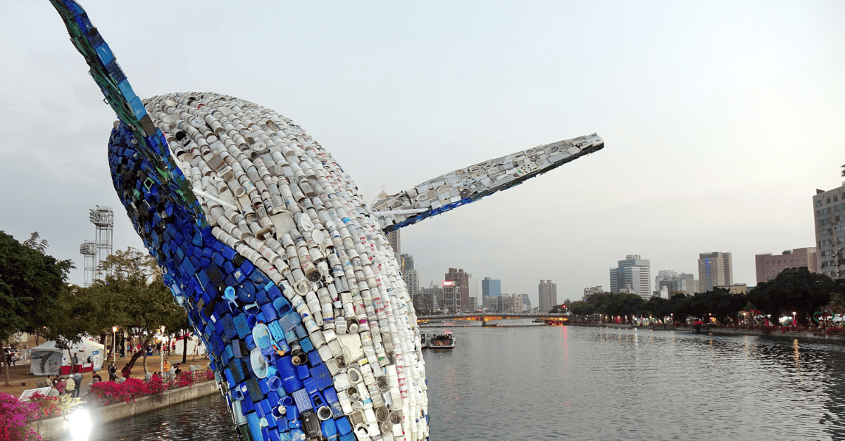 Whale sculpture made from recycled plastic by a waterfront.