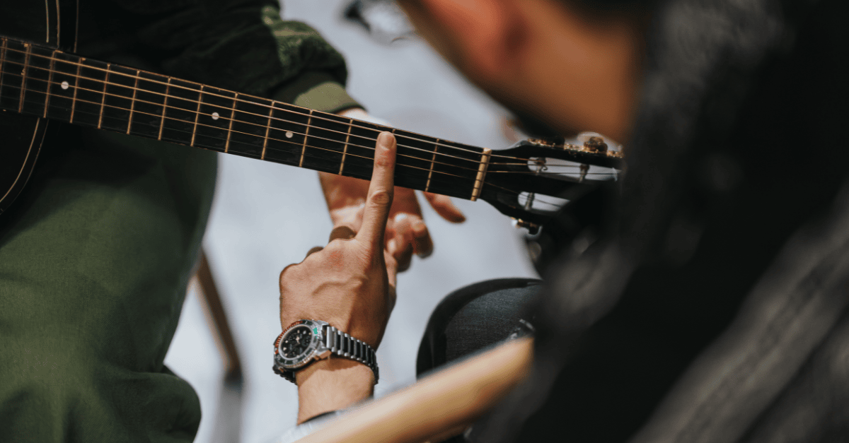 Instructor guides a student playing guitar.