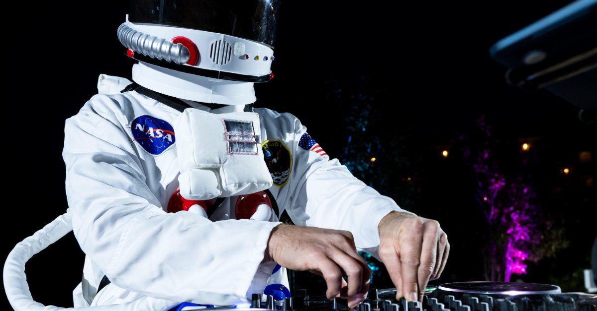 A DJ in an astronaut costume works the turntables at a nighttime outdoor event.