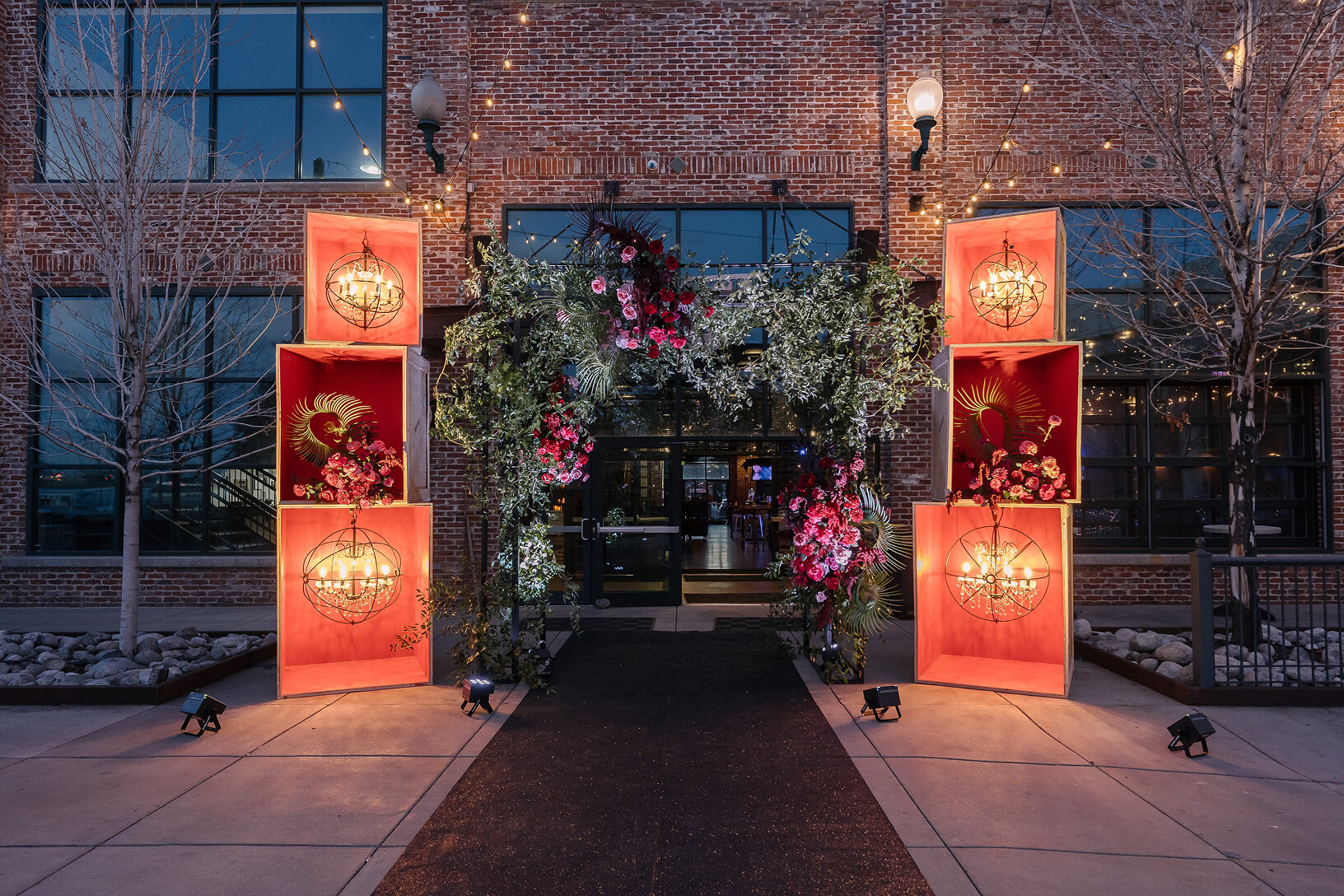 Floral event entrance with illuminated red displays at an industrial venue.