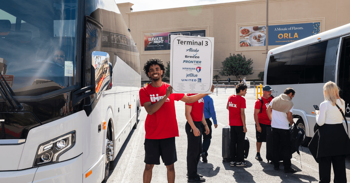 Event staff coordinating transportation beside parked buses, with one person holding a sign at a pickup location.