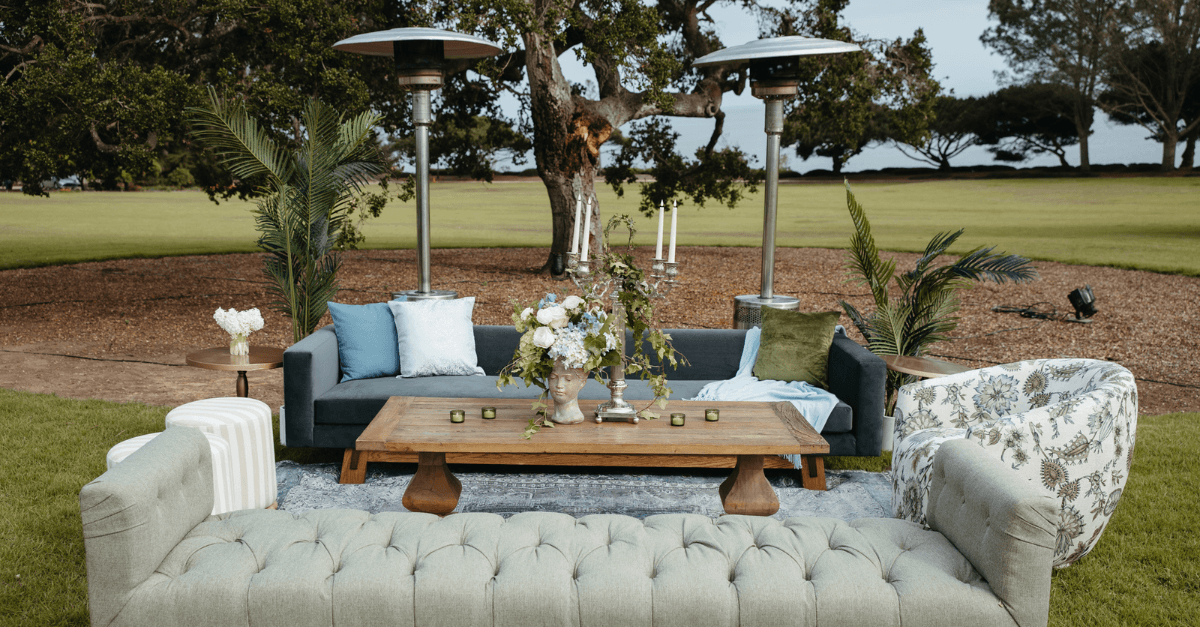 Outdoor lounge setup with sofas, cushions, and patio heaters arranged on a grassy lawn.