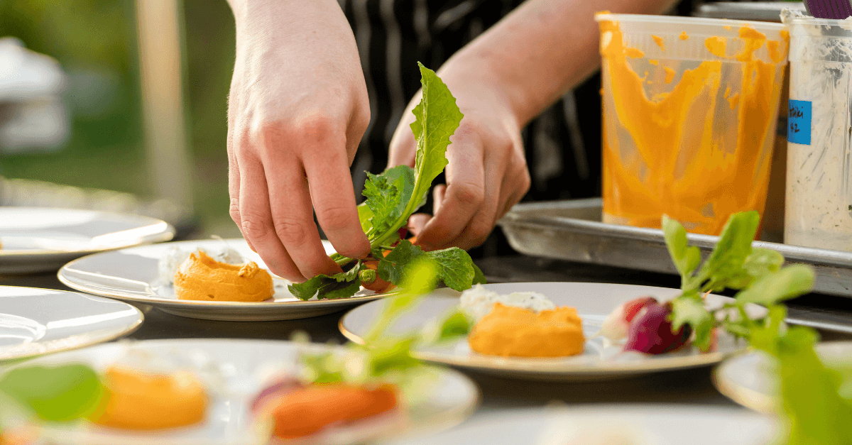 Chef plating dishes with fresh ingredients in an outdoor catering setup.