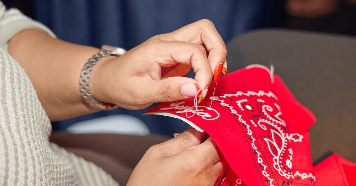 Close-up of hands sewing or crafting a red bandana with white patterns.