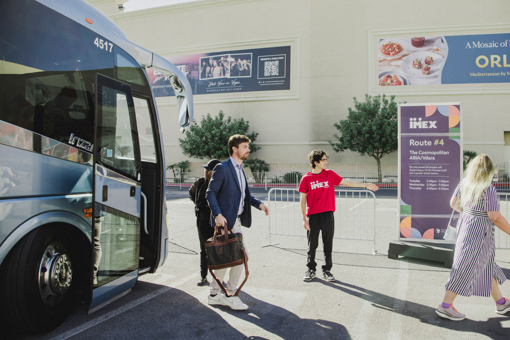 IMEX attendees arrive by shuttle bus as a staff member directs them beside a route sign outside the convention venue.