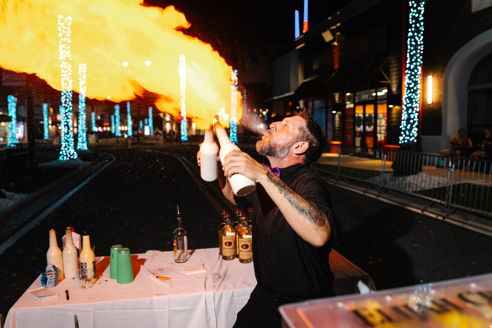 A flare bartender breathes a dramatic stream of fire while preparing drinks at the nighttime block party.