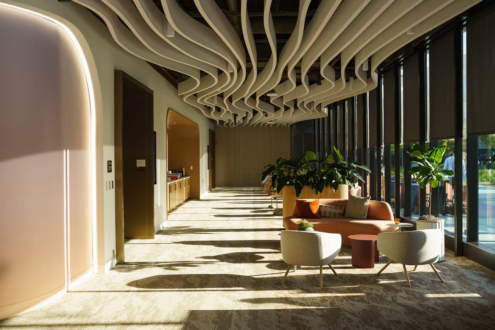 A modern corporate lobby with a curved wood-slat ceiling, lounge seating, and floor-to-ceiling windows.