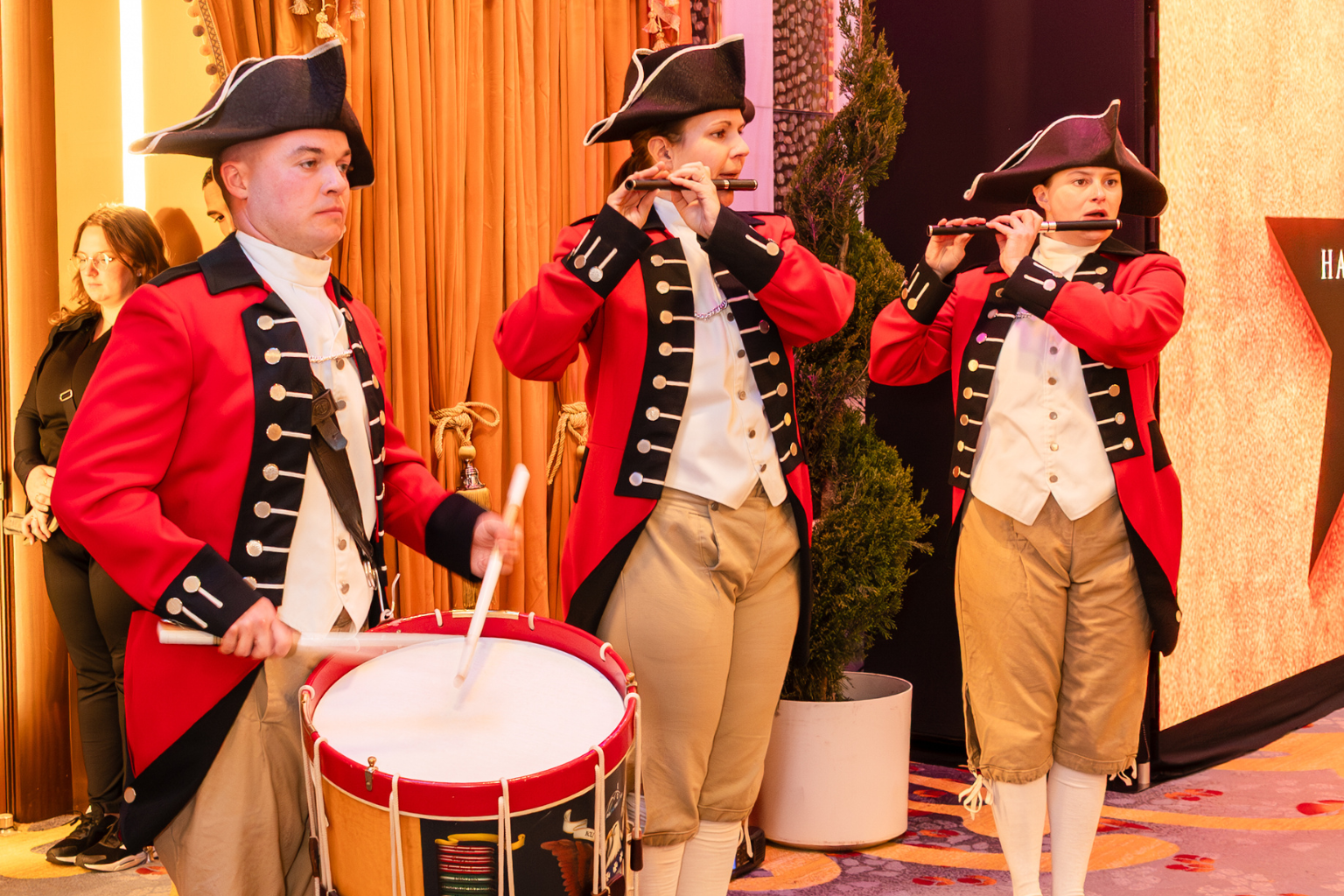 Musicians in colonial-style uniforms playing drums and flutes at a formal event.