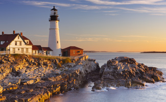 A lighthouse in the Northeast USA sitting on the edge of a peninsula surrounded by water at sunrise